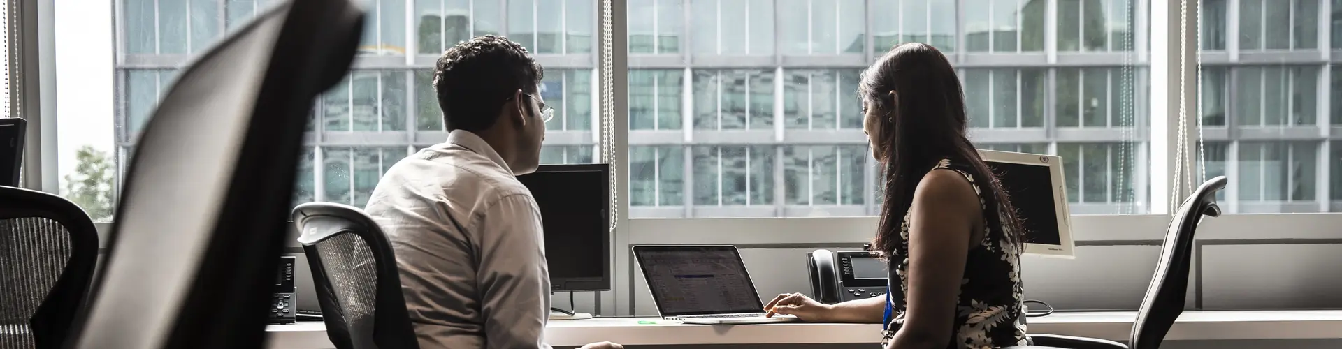 man and woman sitting at a desk facing a laptop screen