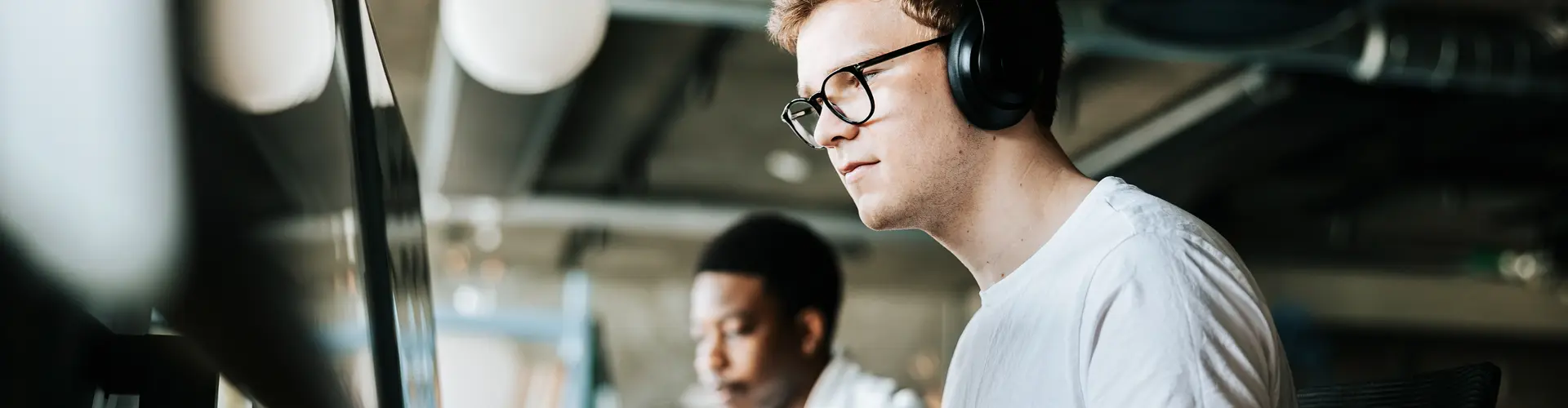 male programmer doing coding on computer with wireless headphones in an office