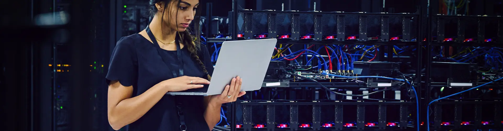 Female technician using a laptop in a server room.