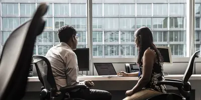 man and woman sitting at a desk facing a laptop screen