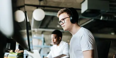 male programmer doing coding on computer with wireless headphones in an office