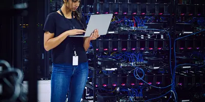 Female technician using a laptop in a server room.