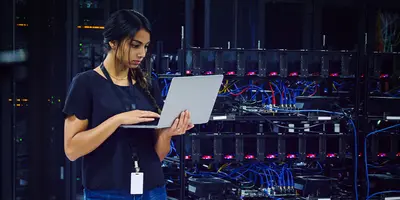 Female technician using a laptop in a server room.