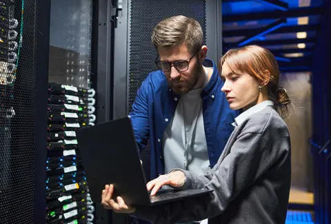 IT professionals are examining server connections in a data center, focusing on laptop screen