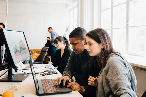 man and woman at desk looking at laptop screen