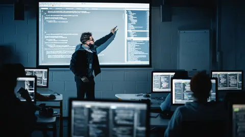 Teacher giving computer science lecture to group of students in dark classroom