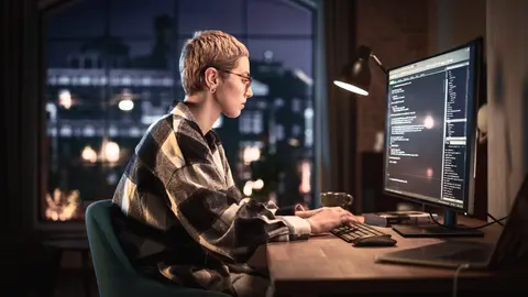 woman sitting at a desk in front of a computer at night looking at monitor