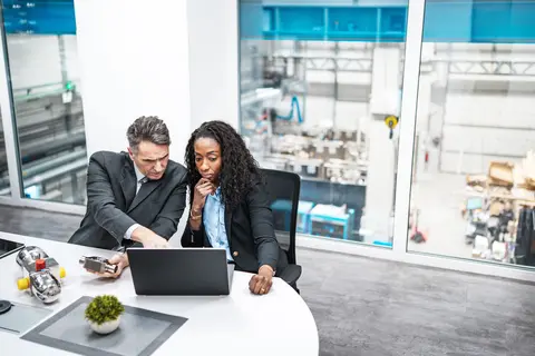 man and woman in a manufacturing office looking at laptop